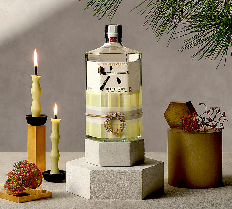 Roku Gin Flasche auf im festlichen Ambiente neben zwei Kerzen und unter einem Zweig
