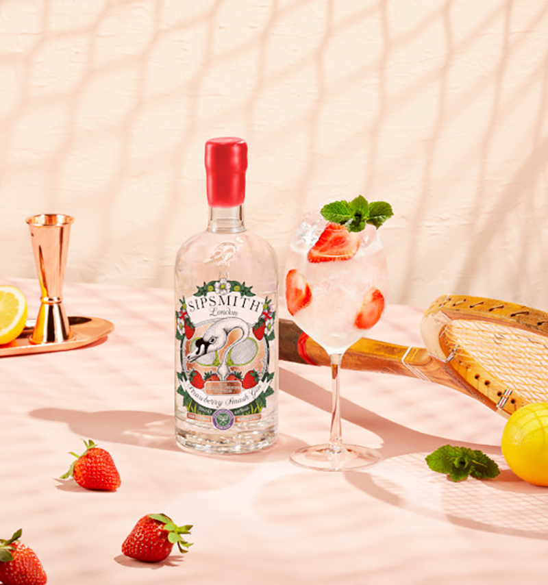 Sipsmith Strawberry Smash Gin Flasche mit Coacktail auf einem tisch mit Erdbeeren und Tennisschläger